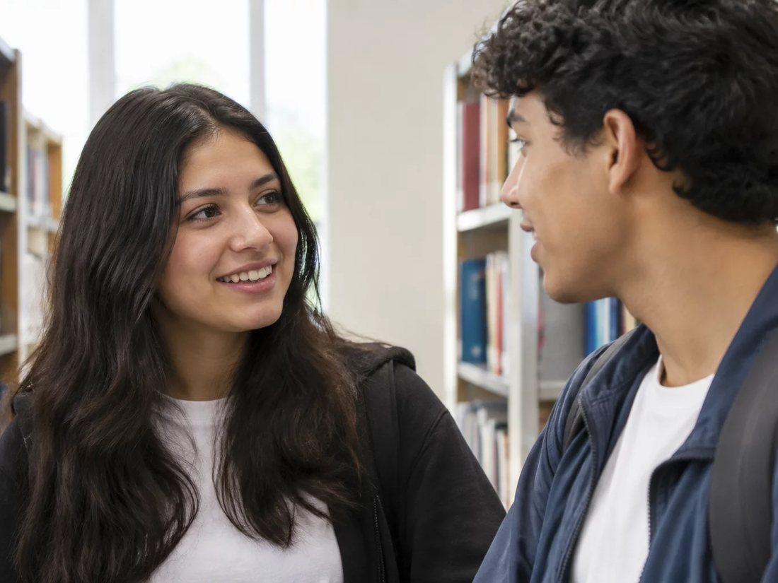 Conversa em pé entre as estantes da escola, com folhas de anotação na mão de quem discute